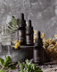 3 black dropper bottles on a stone surface, surrounded by various leaves and sprigs